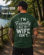 Funny husband t-shirt with "I'm Friendly But My Wife Isn't" back print on a forest green Gildan 5000 unisex tee, humorous men's graphic shirt for husbands, dads, and Father's Day gifts.