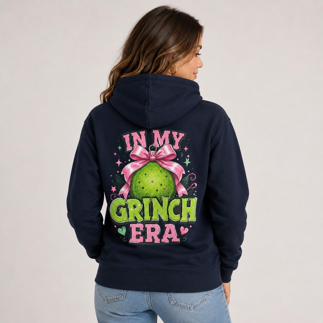 Back view of navy blue hoodie displaying a large In My Grinch Era holiday ornament design with pink and green details.