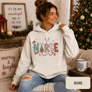 Female model wearing a bone Christmas nurse hoodie with colorful festive NURSE lettering in a cozy holiday living room.