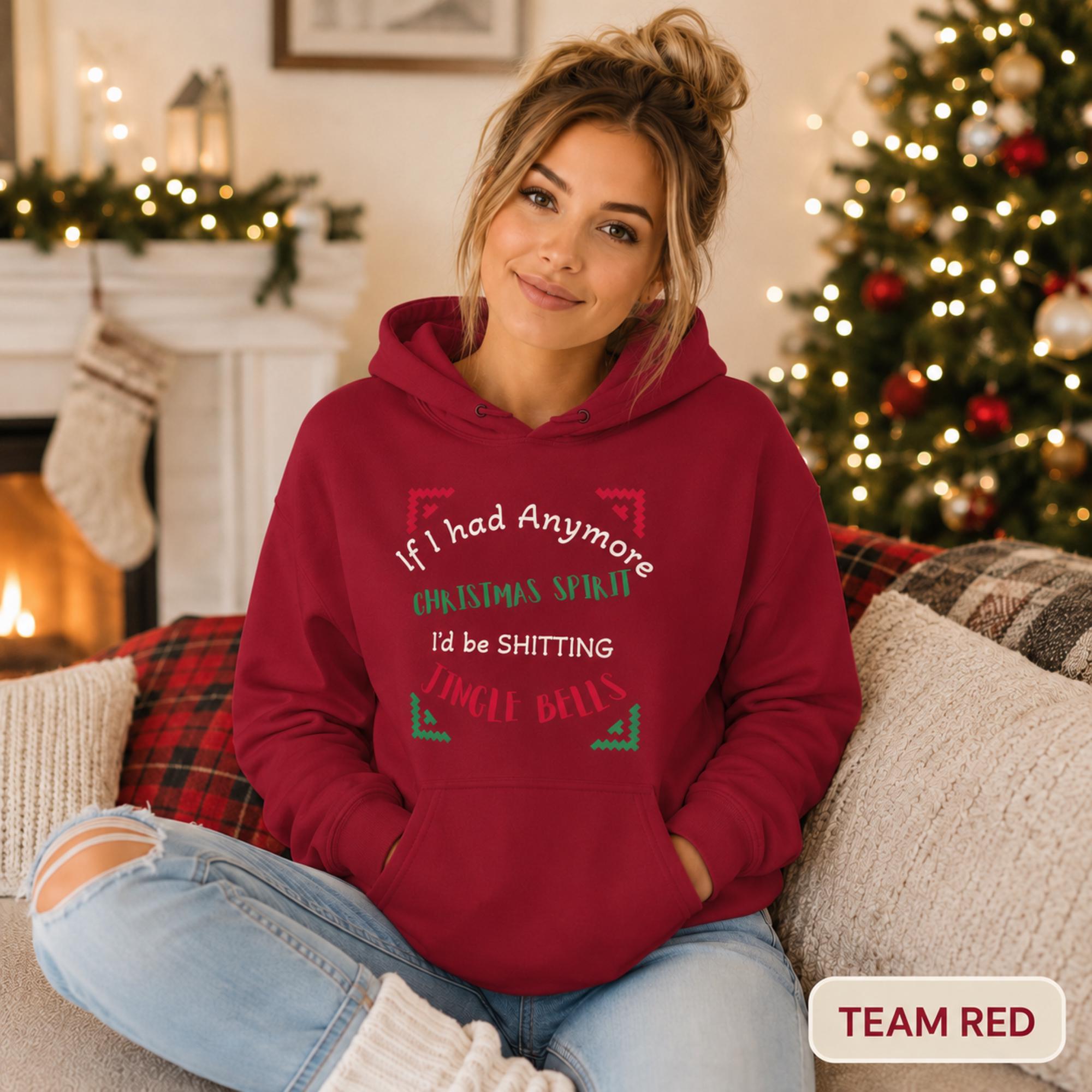 Female model wearing a team red Christmas hoodie reading “If I had anymore Christmas spirit, I’d be shitting jingle bells” in a cozy holiday room.