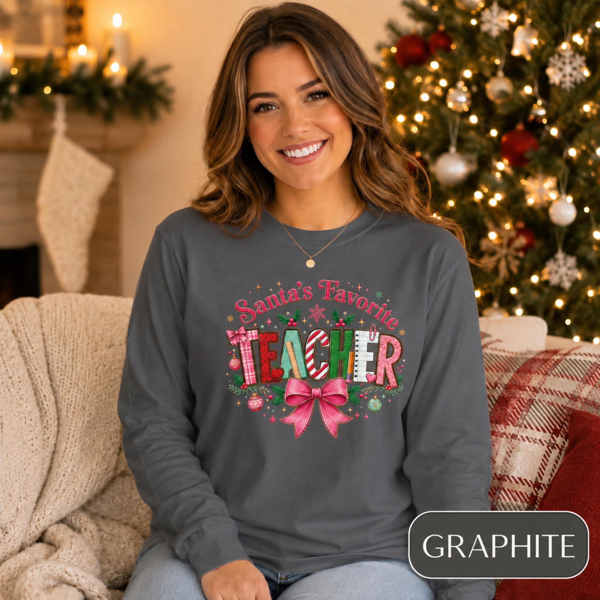 Comfort Colors 6014 long sleeve shirt featuring a colorful Santa’s Favorite Teacher Christmas design with festive lettering, holly, ornaments, school supplies, and a large pink bow.