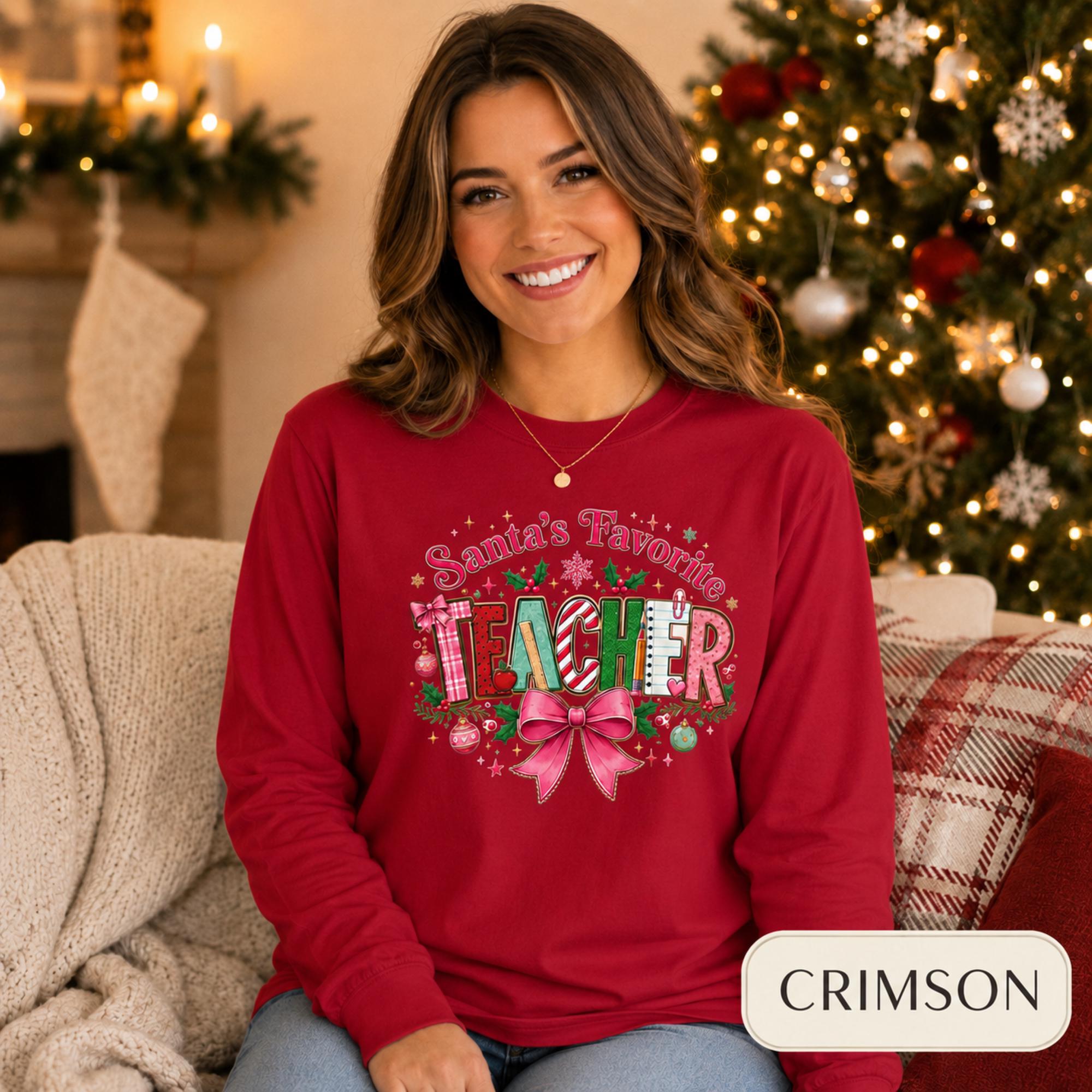 Comfort Colors 6014 long sleeve shirt featuring a colorful Santa’s Favorite Teacher Christmas design with festive lettering, holly, ornaments, school supplies, and a large pink bow.