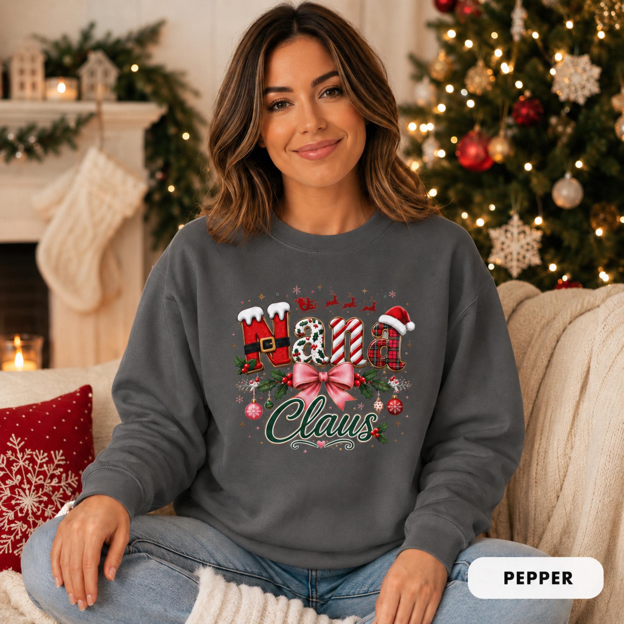 Female model wearing an pepper Comfort Colors crewneck featuring a festive “Nana Claus” Christmas design with a pink bow, holly, ornaments, and holiday lettering.