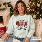 Female model wearing an chalky mint Comfort Colors crewneck featuring a festive “Nana Claus” Christmas design with a pink bow, holly, ornaments, and holiday lettering.