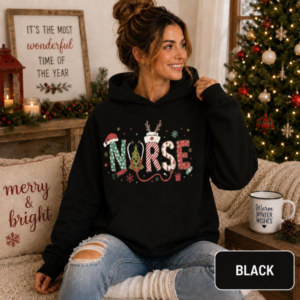Female model wearing a black Christmas nurse hoodie with colorful festive NURSE lettering in a cozy holiday living room.