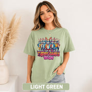 Female model wearing a light green T-shirt with colorful cartoon rabbits and “Let the Tariff Games Begin” graphic design.