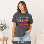 Female model wearing a pepper grey T-shirt featuring cartoon rabbits in sunglasses and “Let the Tariff Games Begin” design.