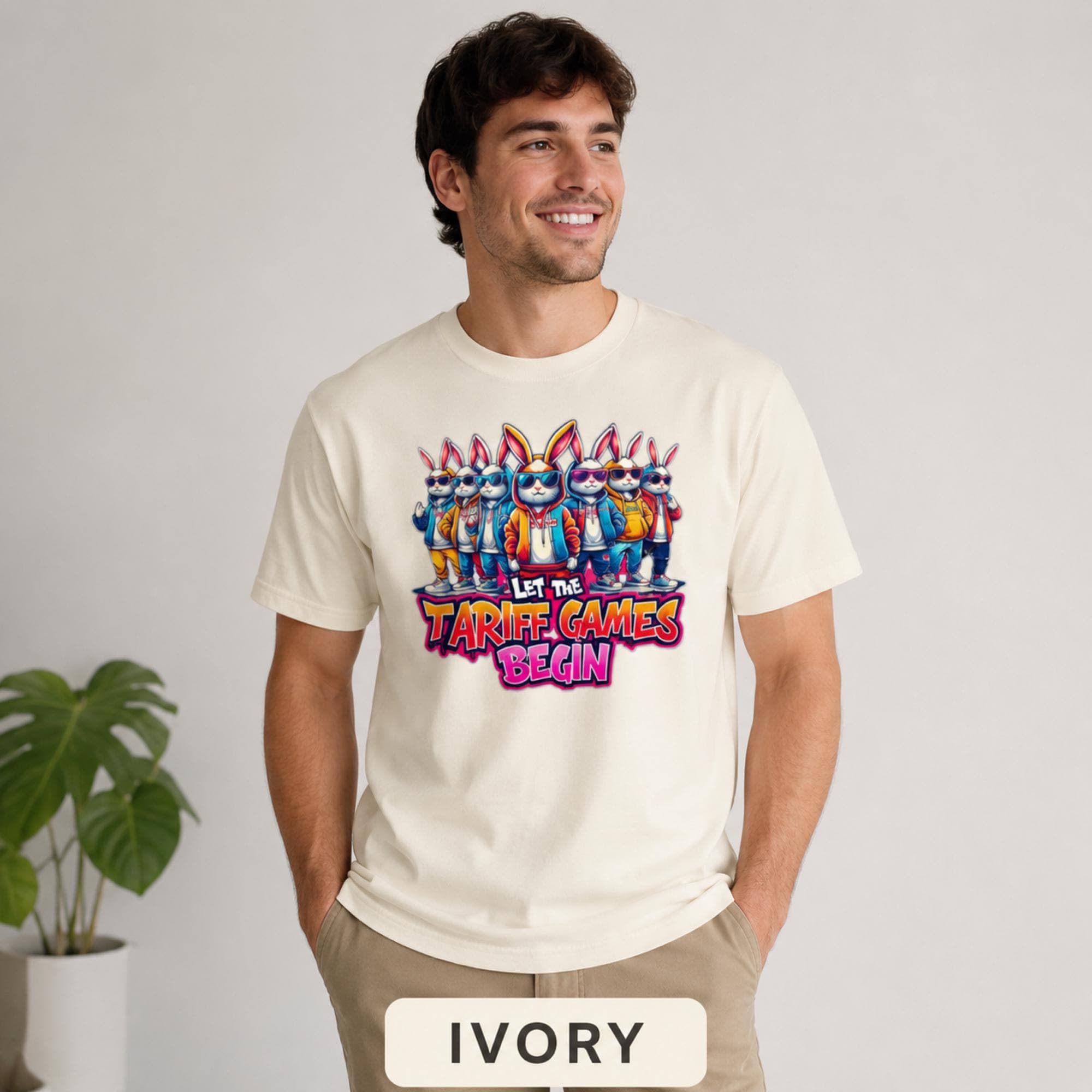 Male model wearing a ivory T-shirt featuring stylish cartoon rabbits and bold “Let the Tariff Games Begin” text.