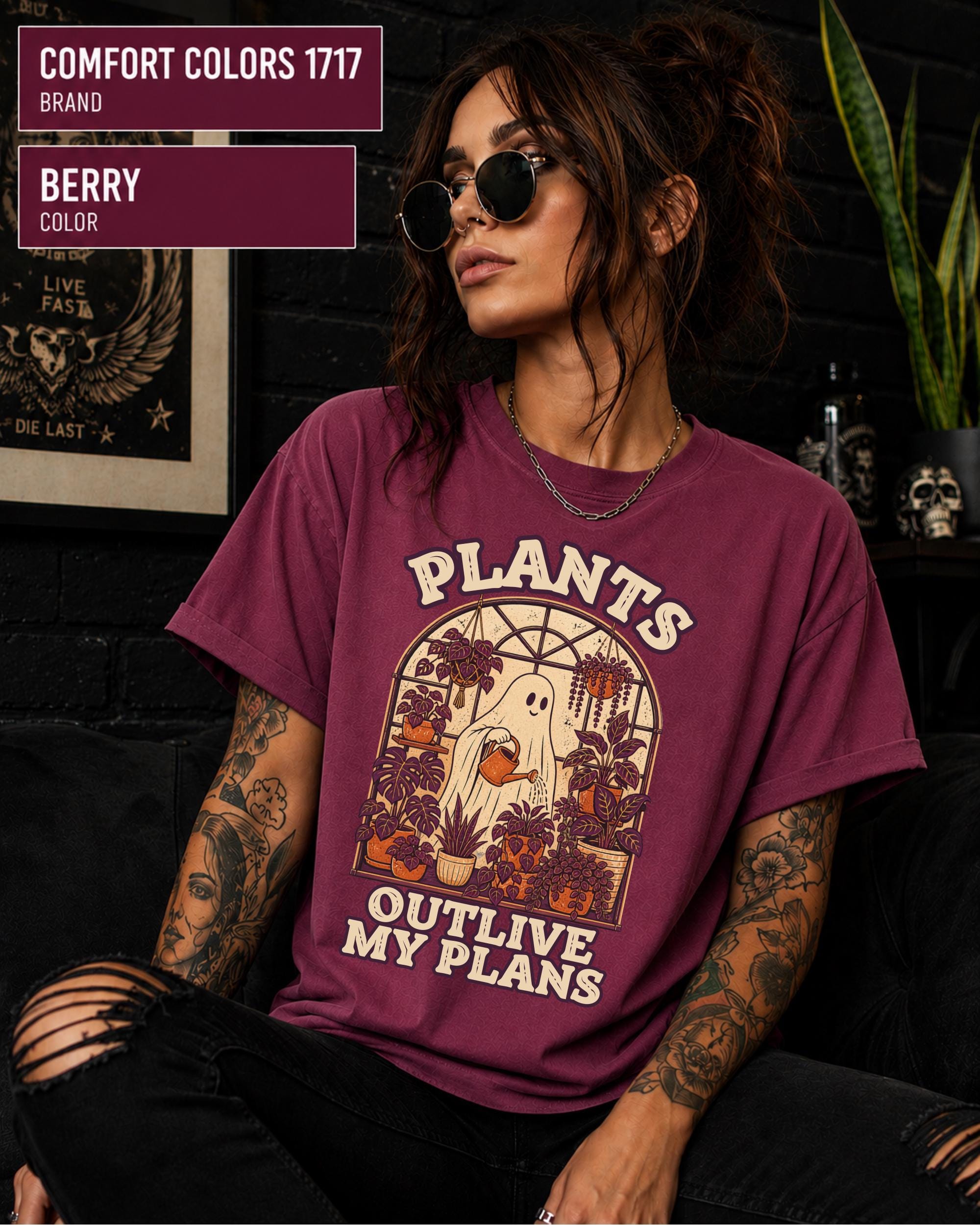 Model wearing Comfort colors tshirt in the color berry featuring a Retro cream and orange ghost watering purple houseplants inside a greenhouse with the words Plants Outlive My Plans.