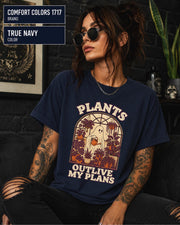 Model wearing Comfort colors tshirt in the color true navy featuring a Retro cream and orange ghost watering purple houseplants inside a greenhouse with the words Plants Outlive My Plans.