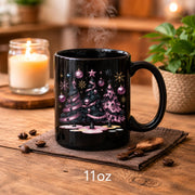 Black ceramic coffee cup displaying spooky Christmas tree design with pink ornaments.