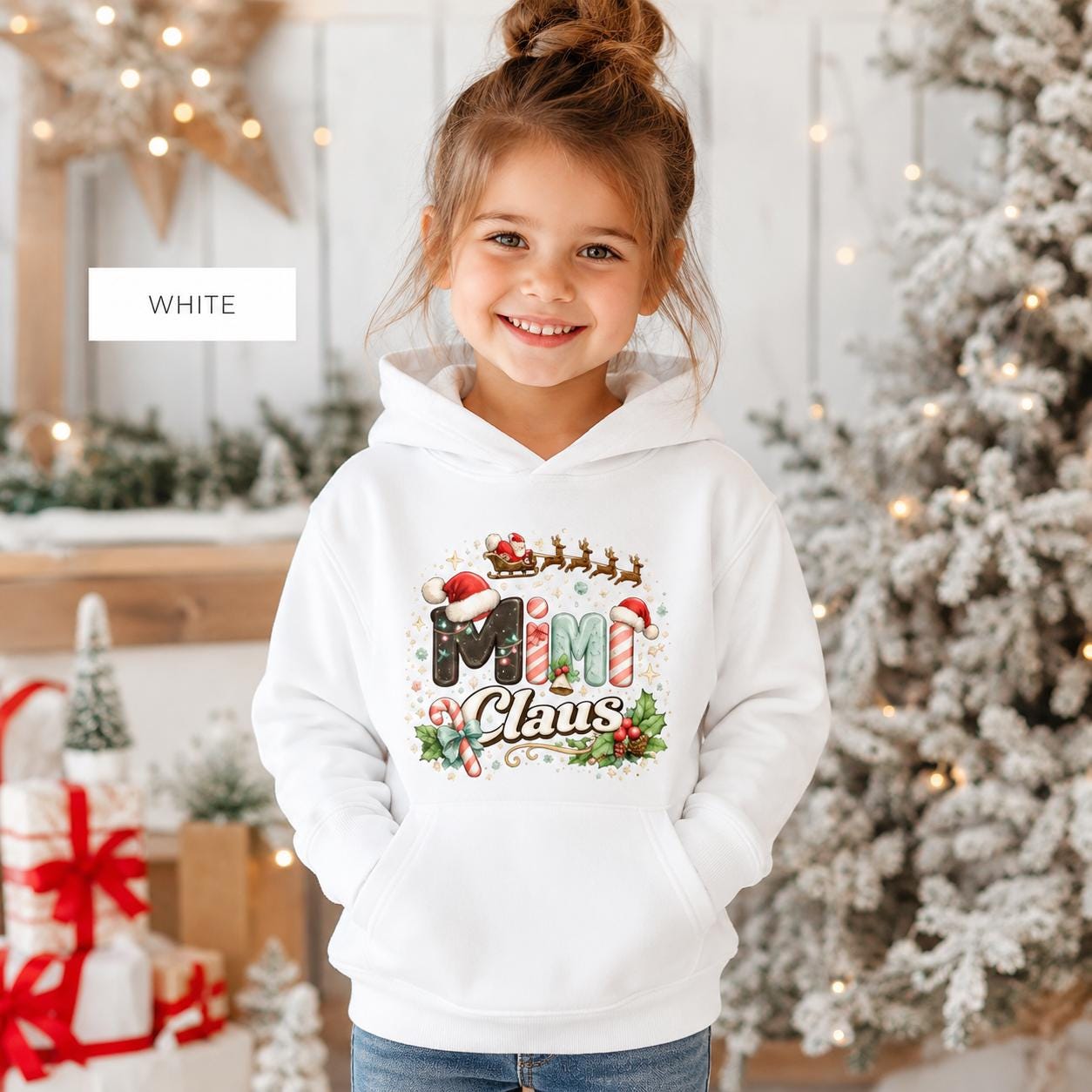 Young girl wearing a white Mini Claus Christmas hoodie with festive holiday artwork.