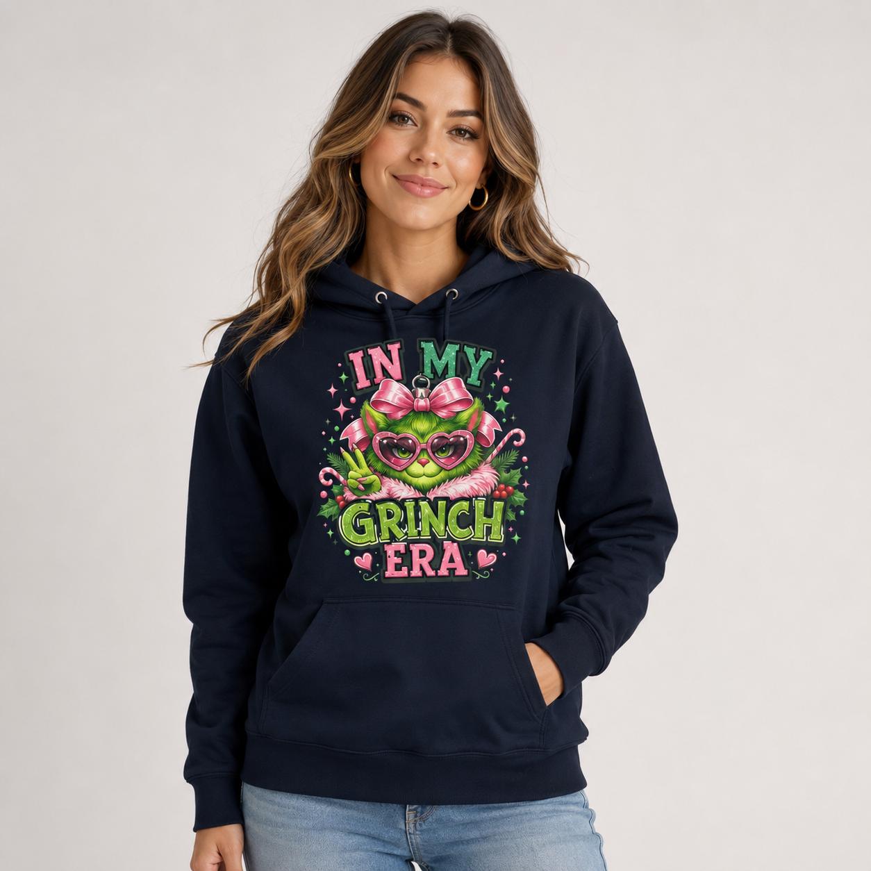 Front view of navy blue hoodie displaying a large In My Grinch Era holiday ornament design with pink and green details.