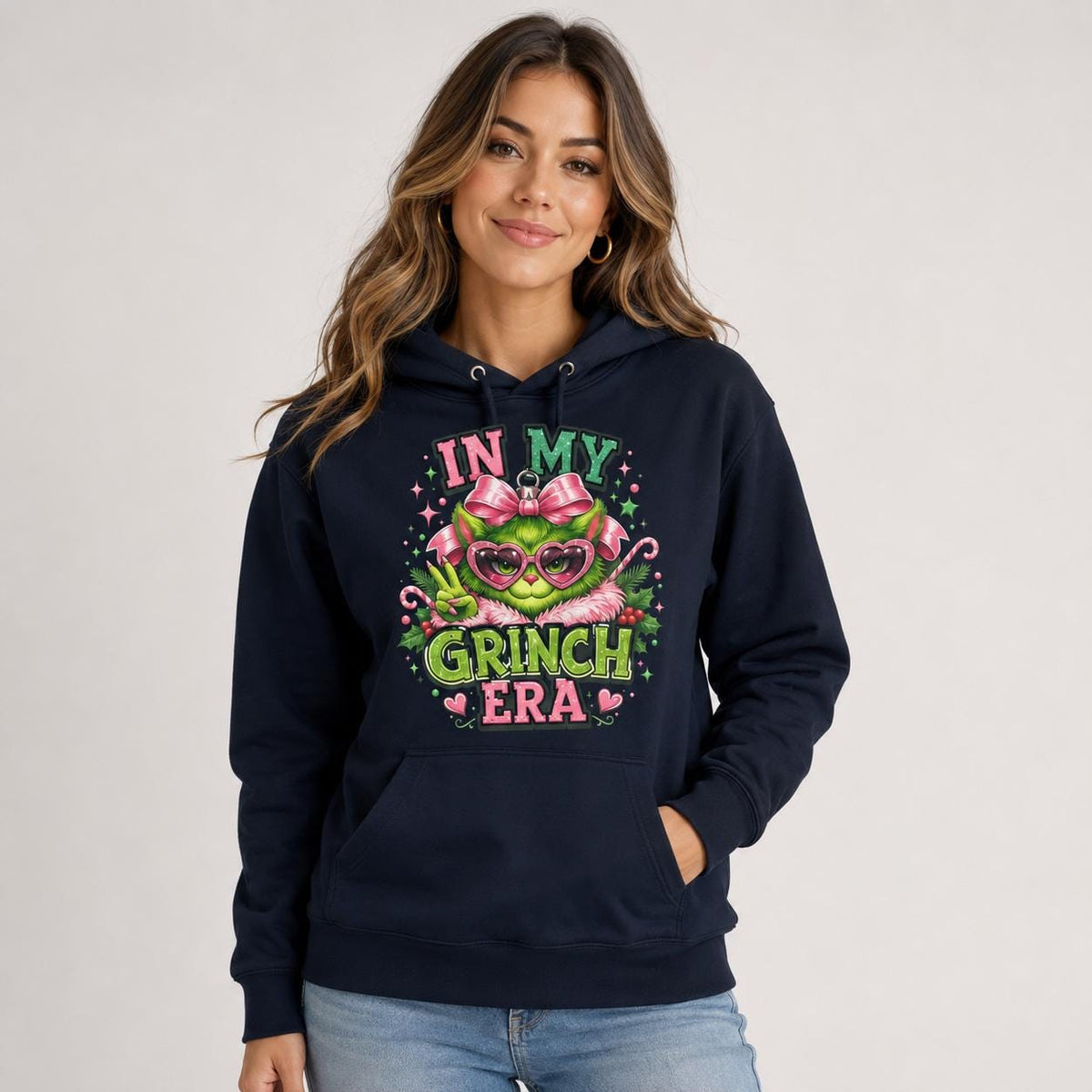 Front view of navy blue hoodie displaying a large In My Grinch Era holiday ornament design with pink and green details.