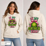 Female model wearing a bone-colored hoodie with a bright pink and green holiday character design printed on the front & back.