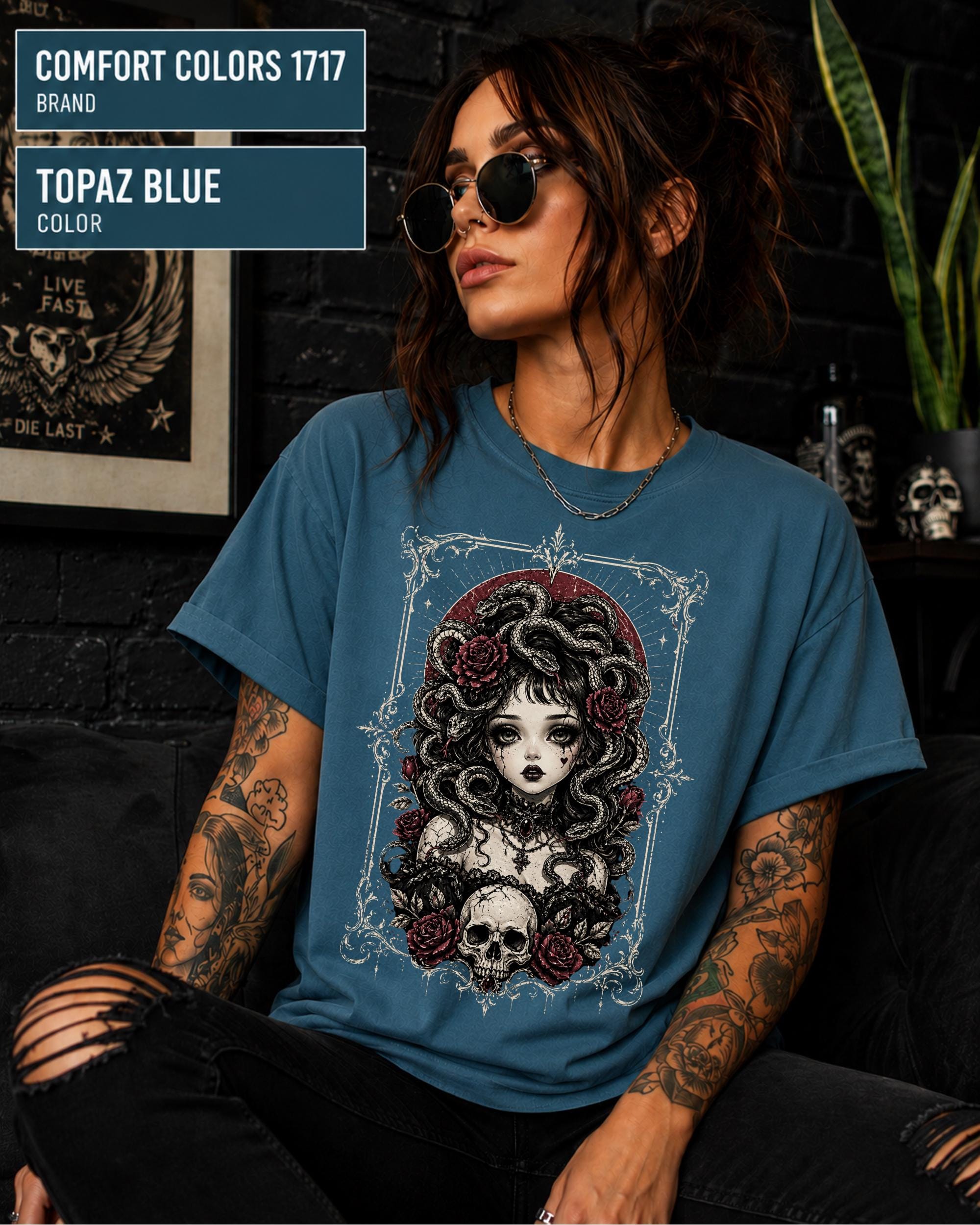 Woman wearing a Topaz Blue Comfort Colors 1717 T-shirt featuring a gothic Medusa-inspired woman with snakes, dark roses, ornate framing, and a skull design.
