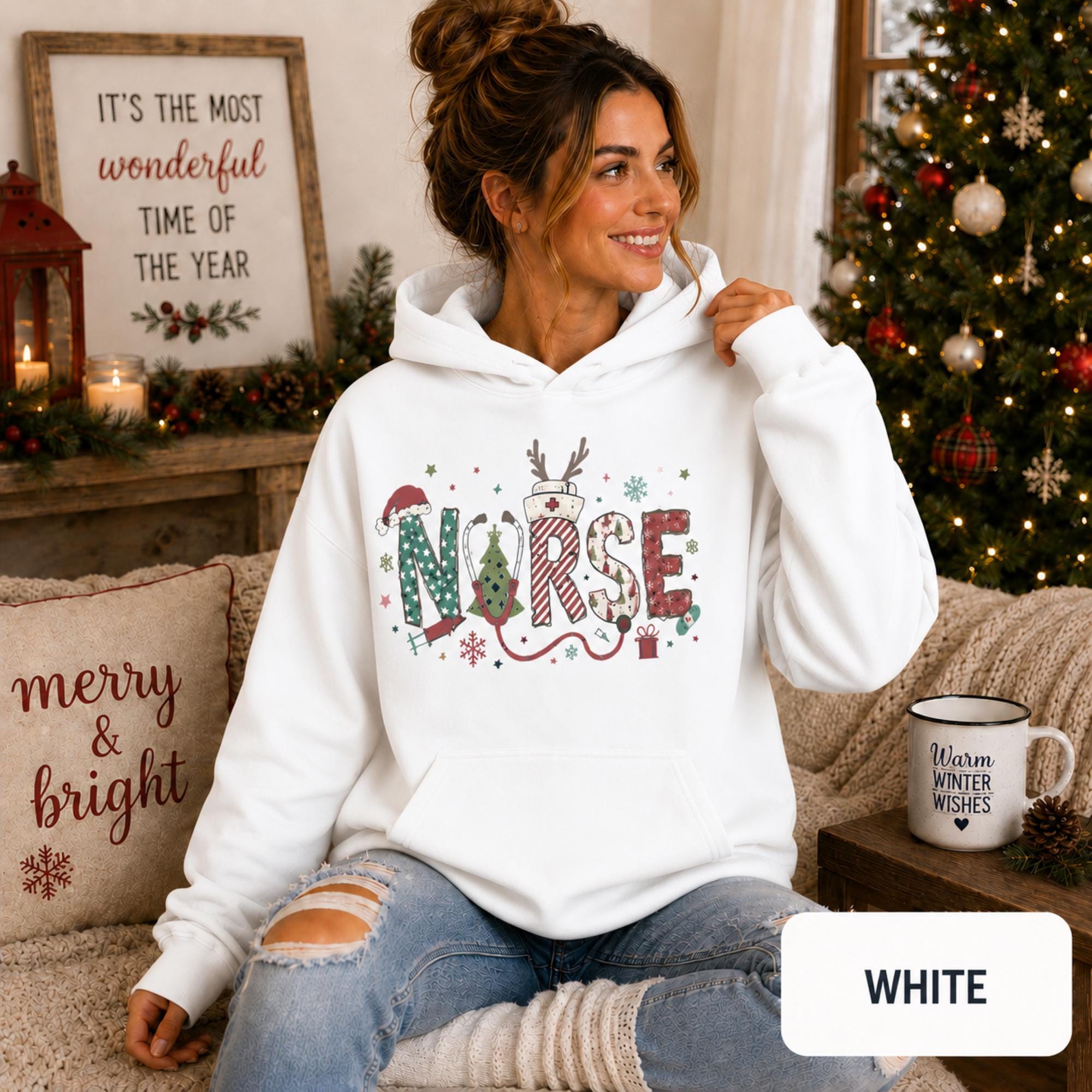 Female model wearing a white Christmas nurse hoodie with colorful festive NURSE lettering in a cozy holiday living room.