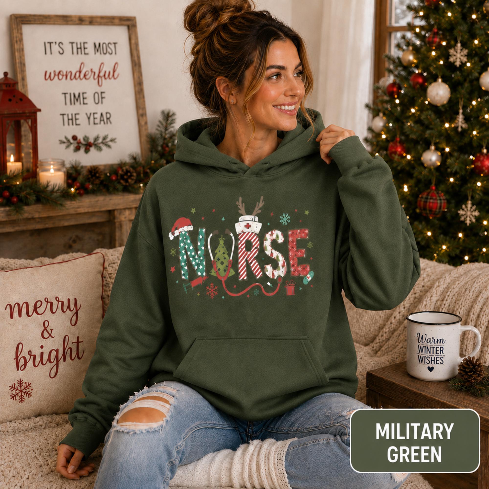 Female model wearing a military green Christmas nurse hoodie with colorful festive NURSE lettering in a cozy holiday living room.