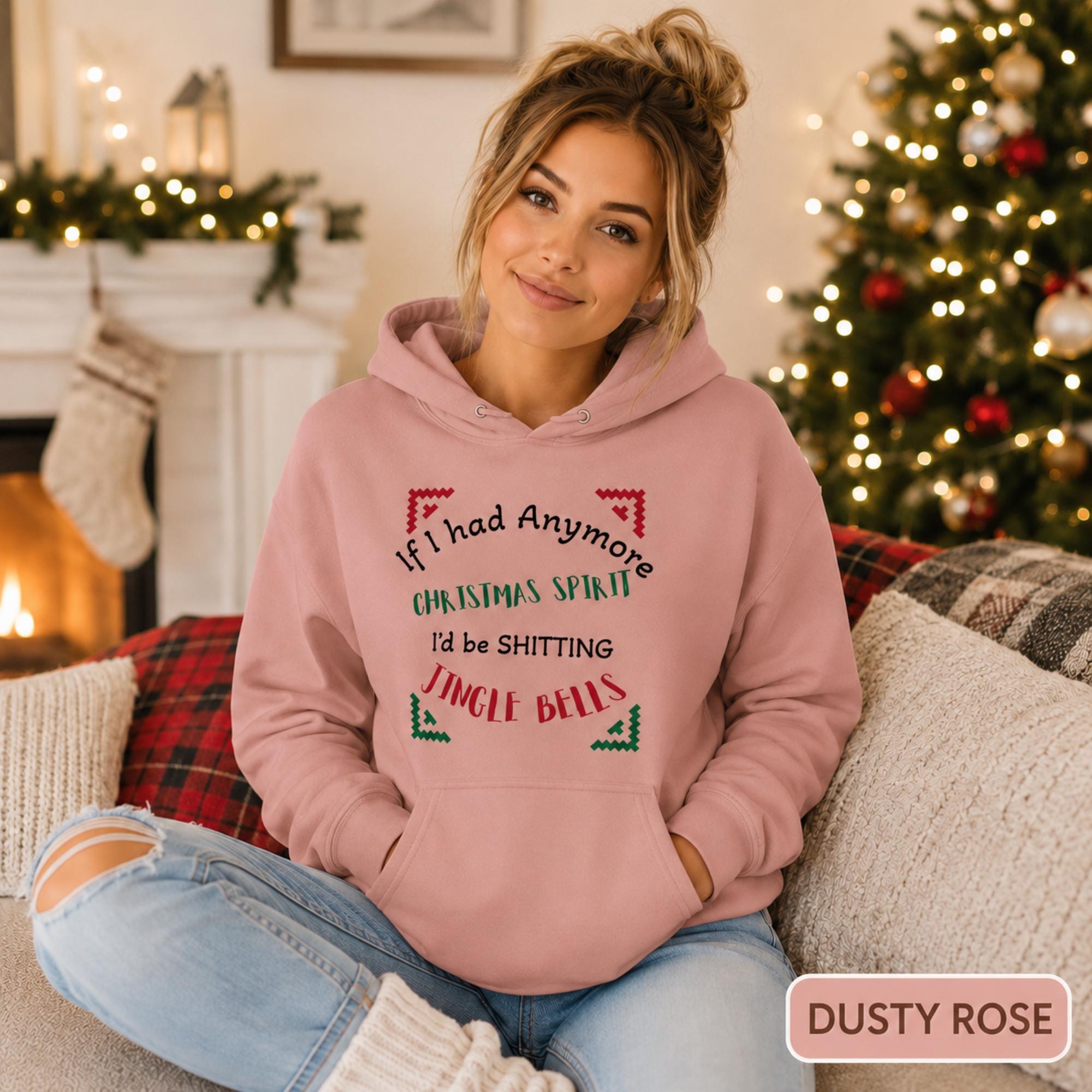 Female model wearing a dusty rose Christmas hoodie reading “If I had anymore Christmas spirit, I’d be shitting jingle bells” in a cozy holiday room.
