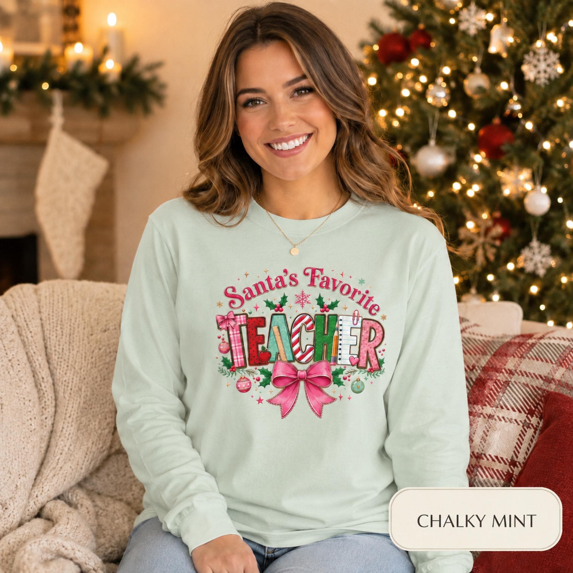 Comfort Colors 6014 long sleeve shirt featuring a colorful Santa’s Favorite Teacher Christmas design with festive lettering, holly, ornaments, school supplies, and a large pink bow.