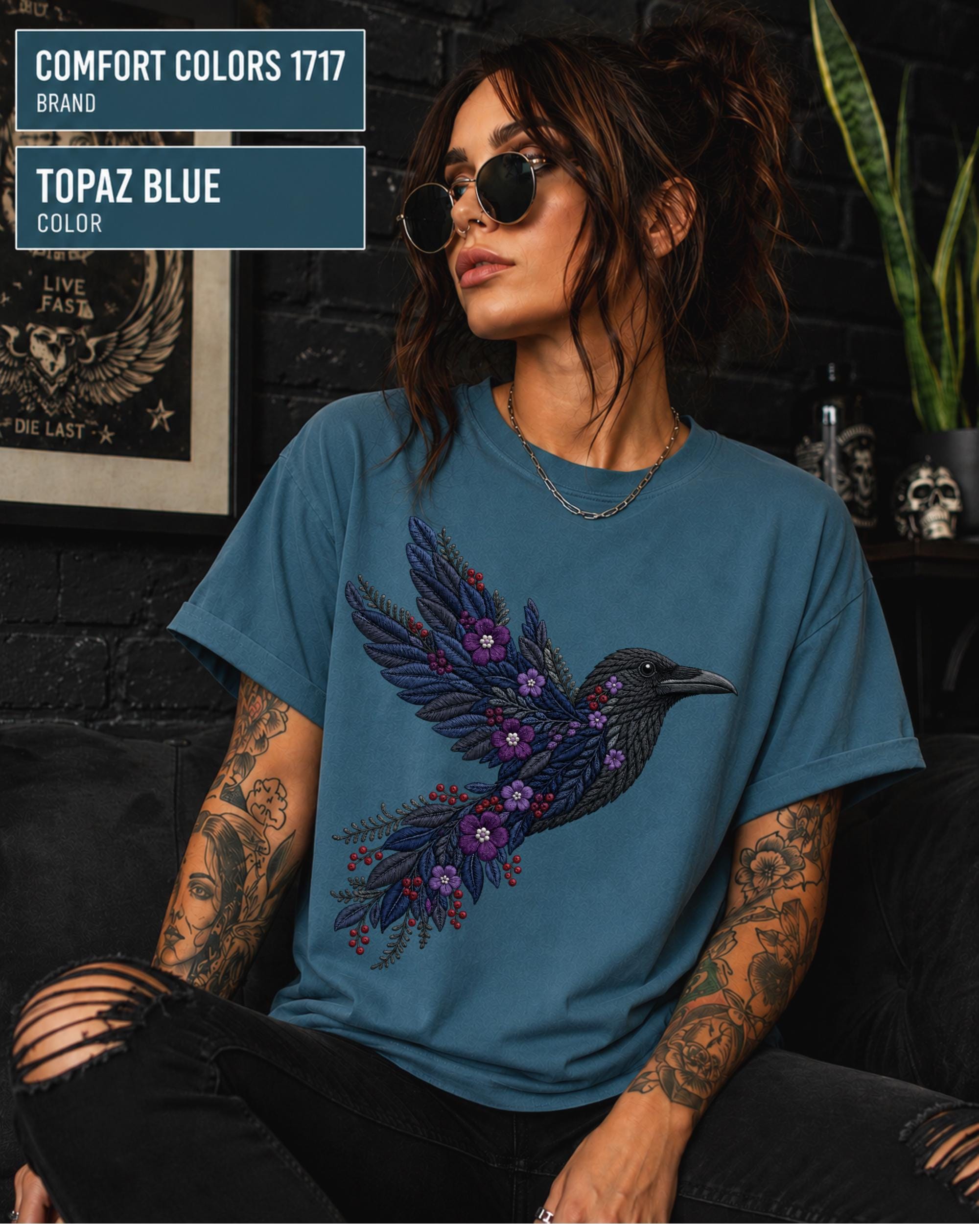 Topaz Blue Comfort Colors 1717 t-shirt featuring a black raven graphic with purple flowers and blue feather details in a gothic botanical style.
