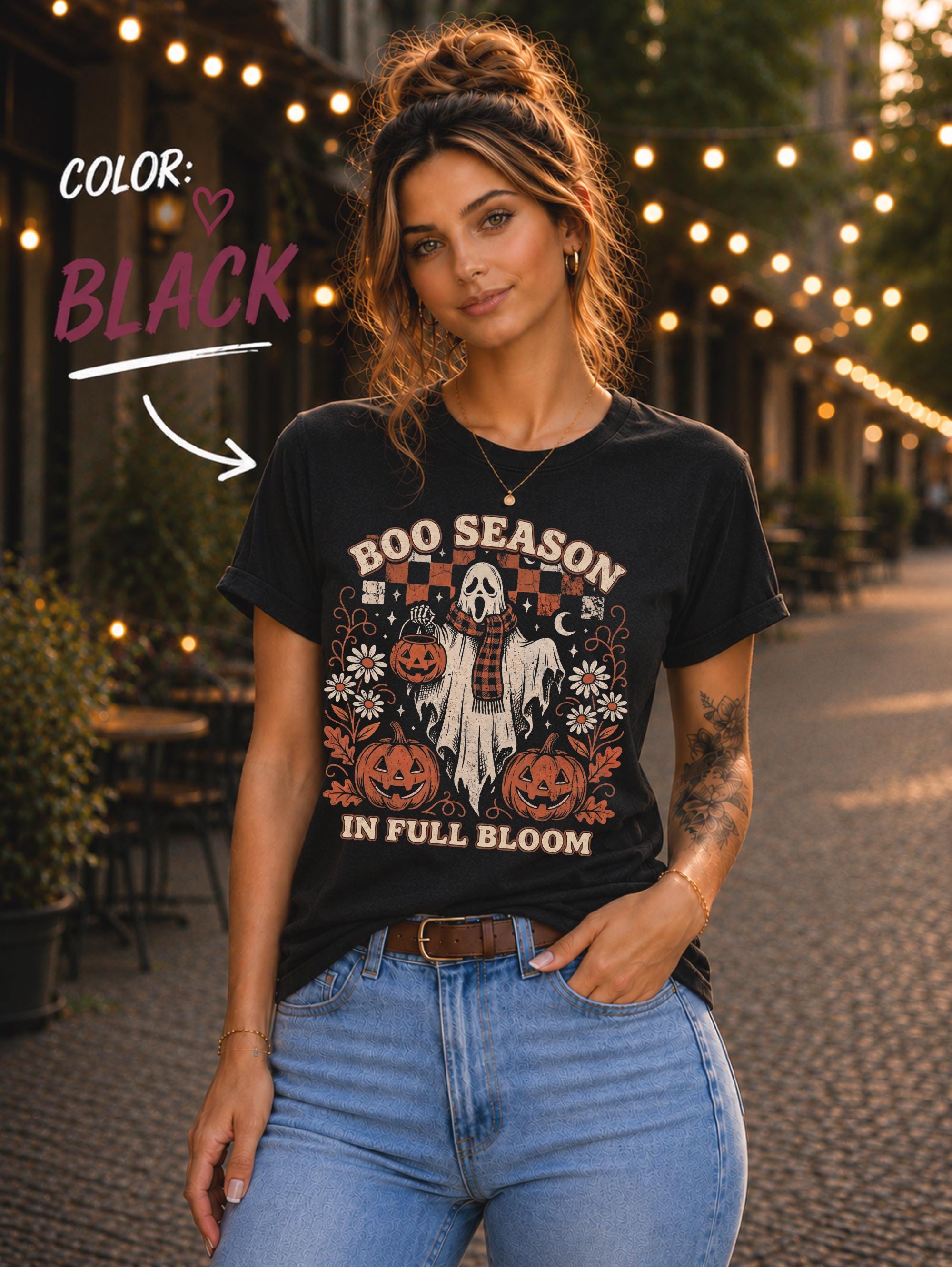 Woman wearing a black Boo Season in Full Bloom Halloween shirt featuring a ghost, pumpkins, daisies, and retro orange artwork.