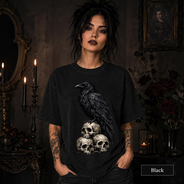 Woman wearing a Black Comfort Colors 1717 shirt featuring a black raven perched on three weathered skulls.