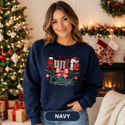 Holiday crewneck with Auntie Claus design shown in navy against a decorated Christmas tree background.