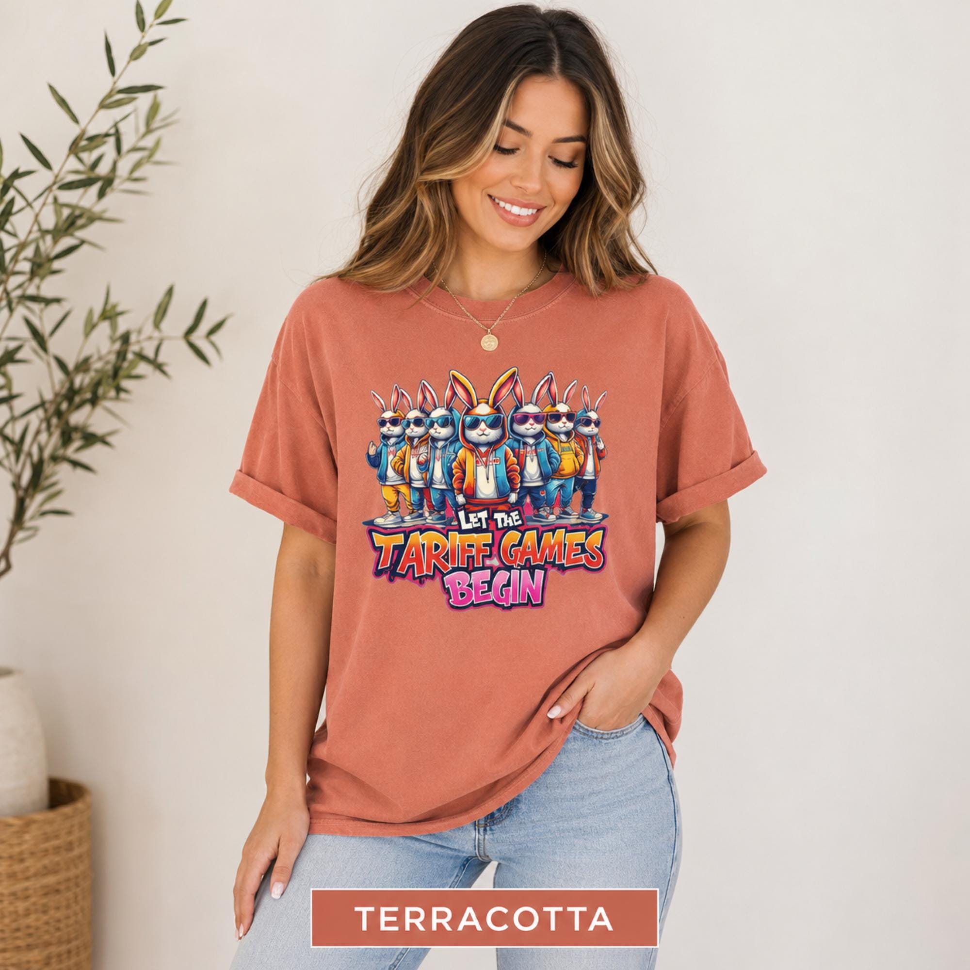 Female model wearing a terracotta T-shirt with colorful streetwear-style rabbits and bold tariff games graphic.