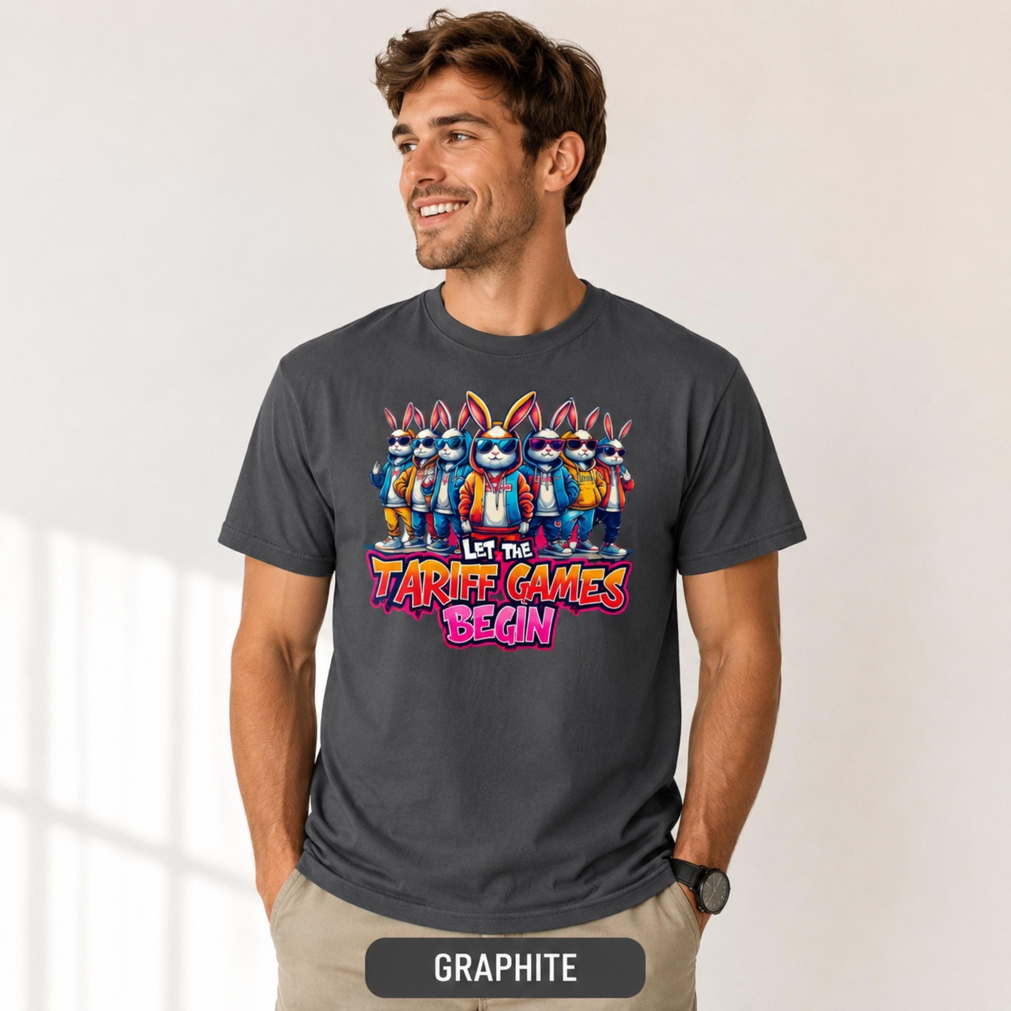 Male model wearing a graphite T-shirt featuring stylish cartoon rabbits and bold “Let the Tariff Games Begin” text.