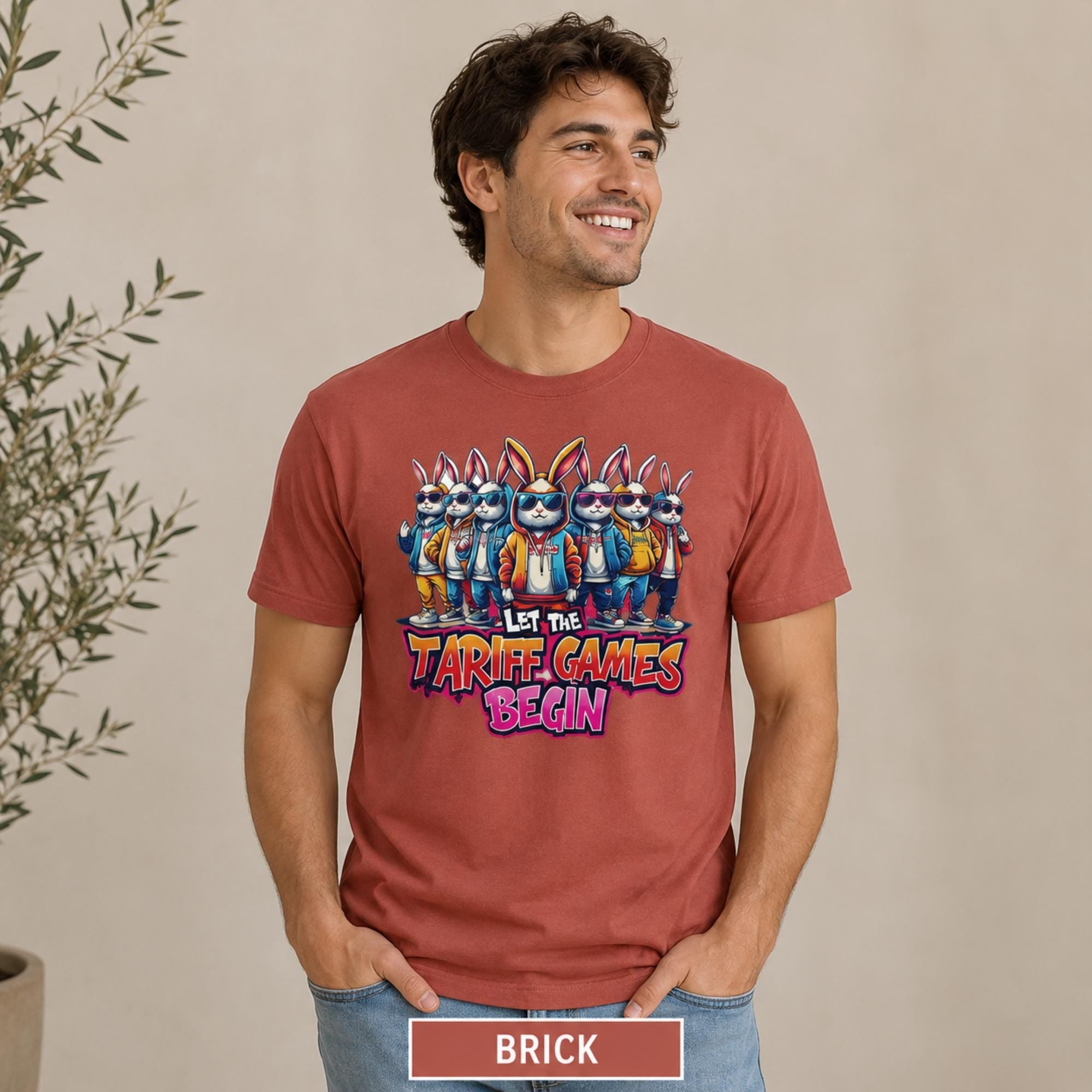 Male model wearing a brick T-shirt featuring stylish cartoon rabbits and bold “Let the Tariff Games Begin” text.