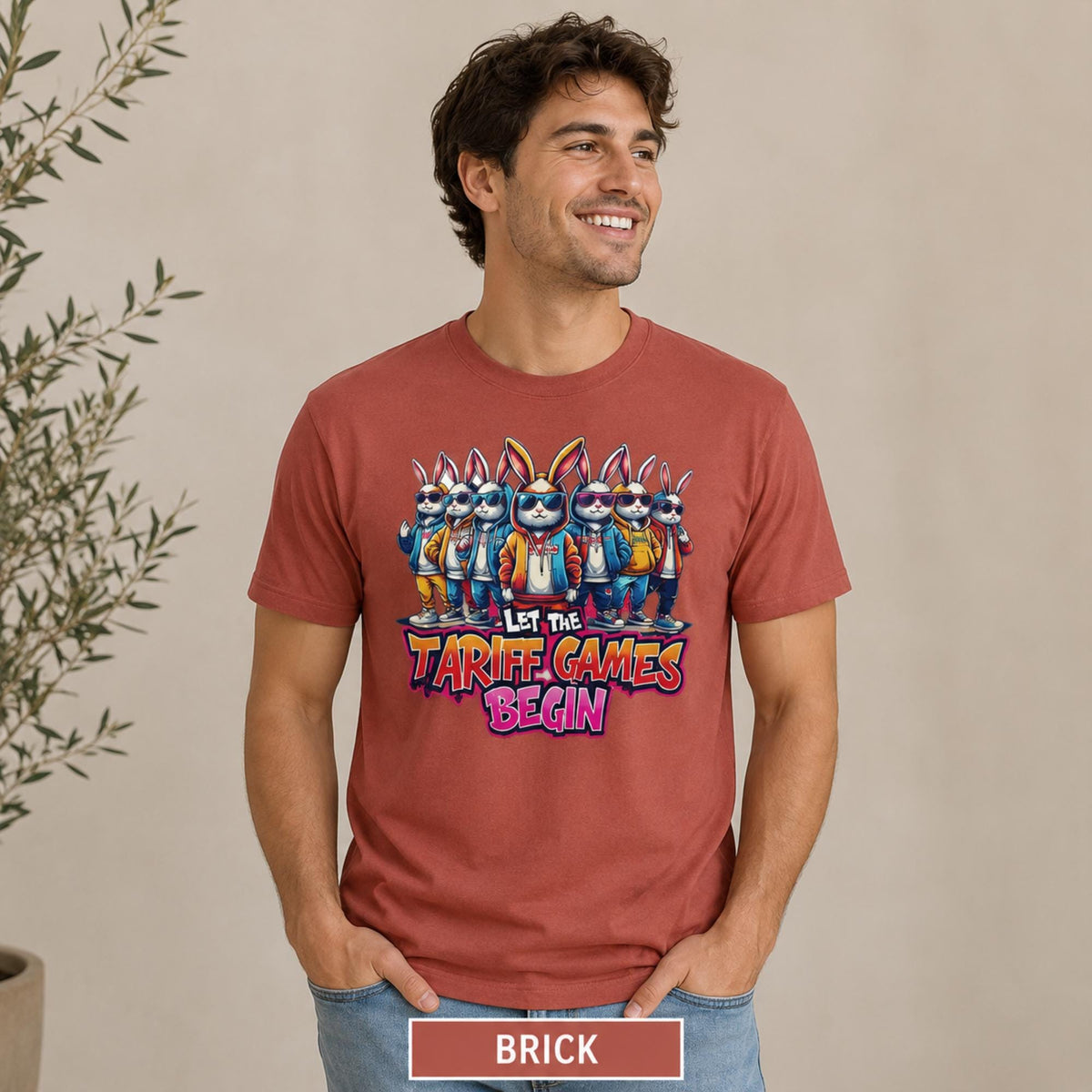 Male model wearing a brick T-shirt featuring stylish cartoon rabbits and bold “Let the Tariff Games Begin” text.