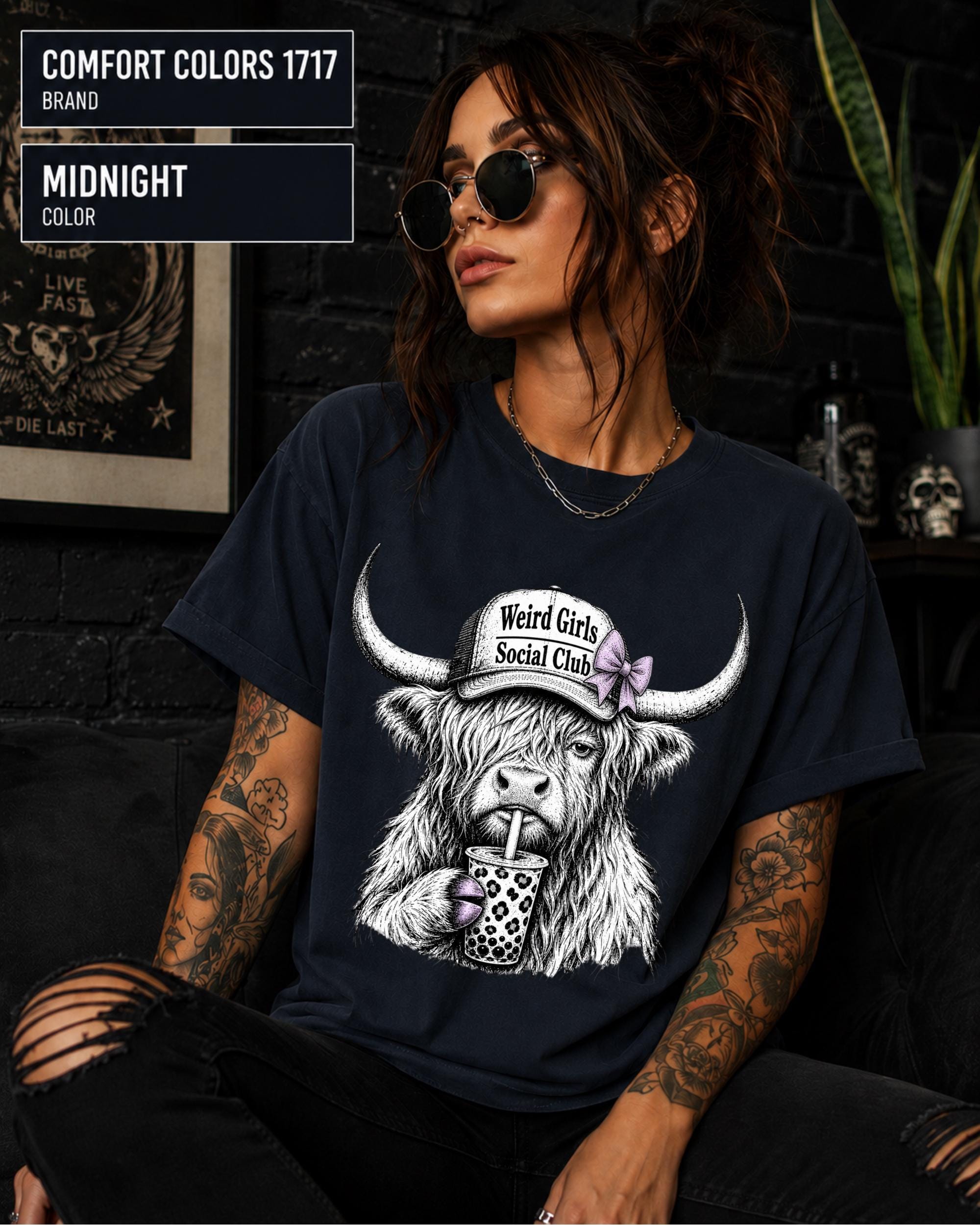Woman wearing a Midnight Comfort Colors 1717 shirt featuring a Highland cow with a Weird Girls Social Club hat and boba drink.