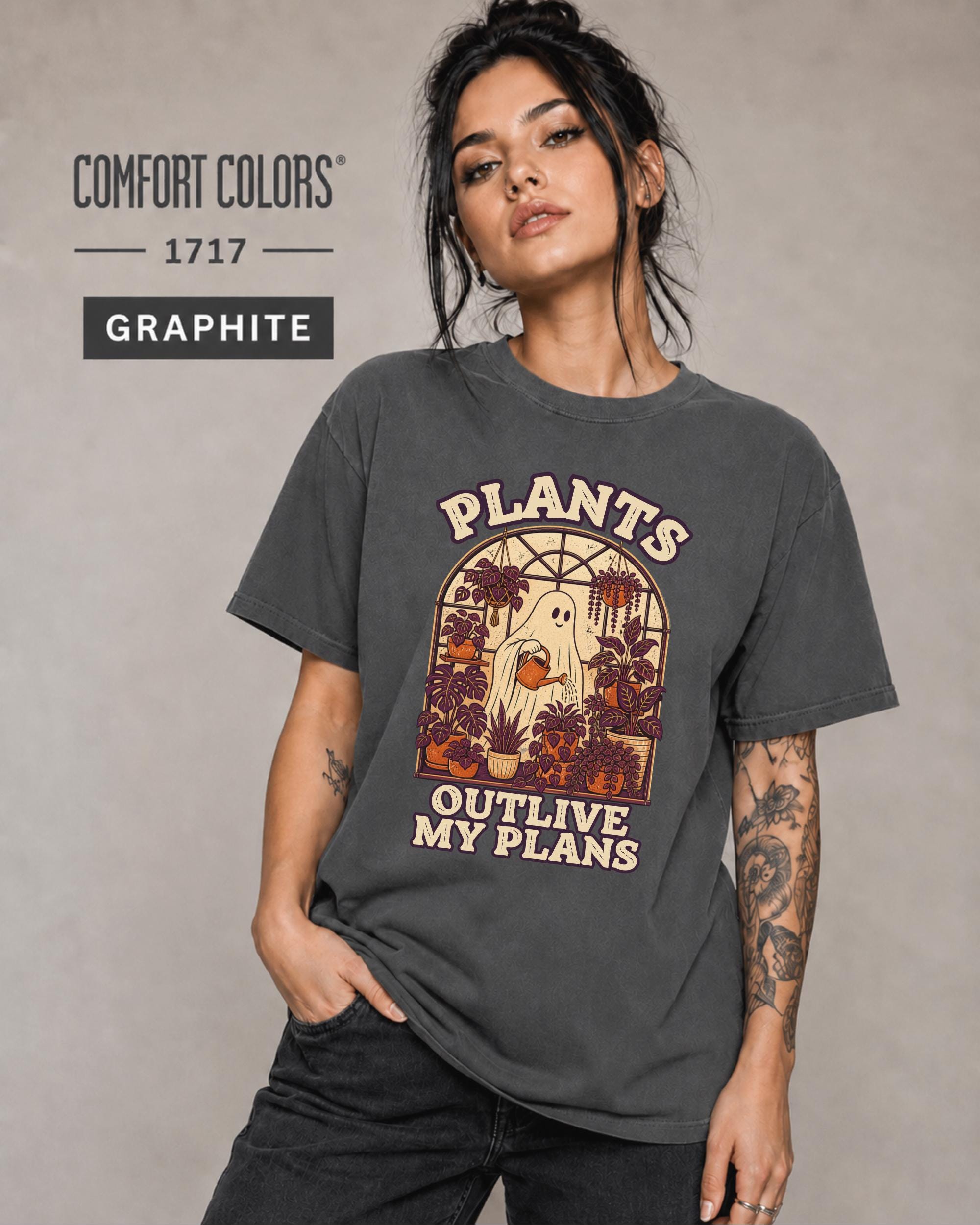 Model wearing Comfort colors tshirt in the color graphite featuring a Retro cream and orange ghost watering purple houseplants inside a greenhouse with the words Plants Outlive My Plans.