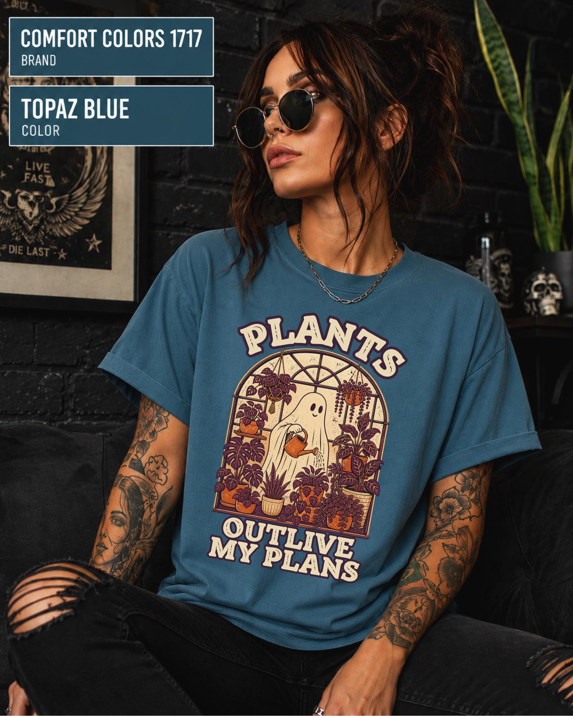 Model wearing Comfort colors tshirt in the color topez blue featuring a Retro cream and orange ghost watering purple houseplants inside a greenhouse with the words Plants Outlive My Plans.