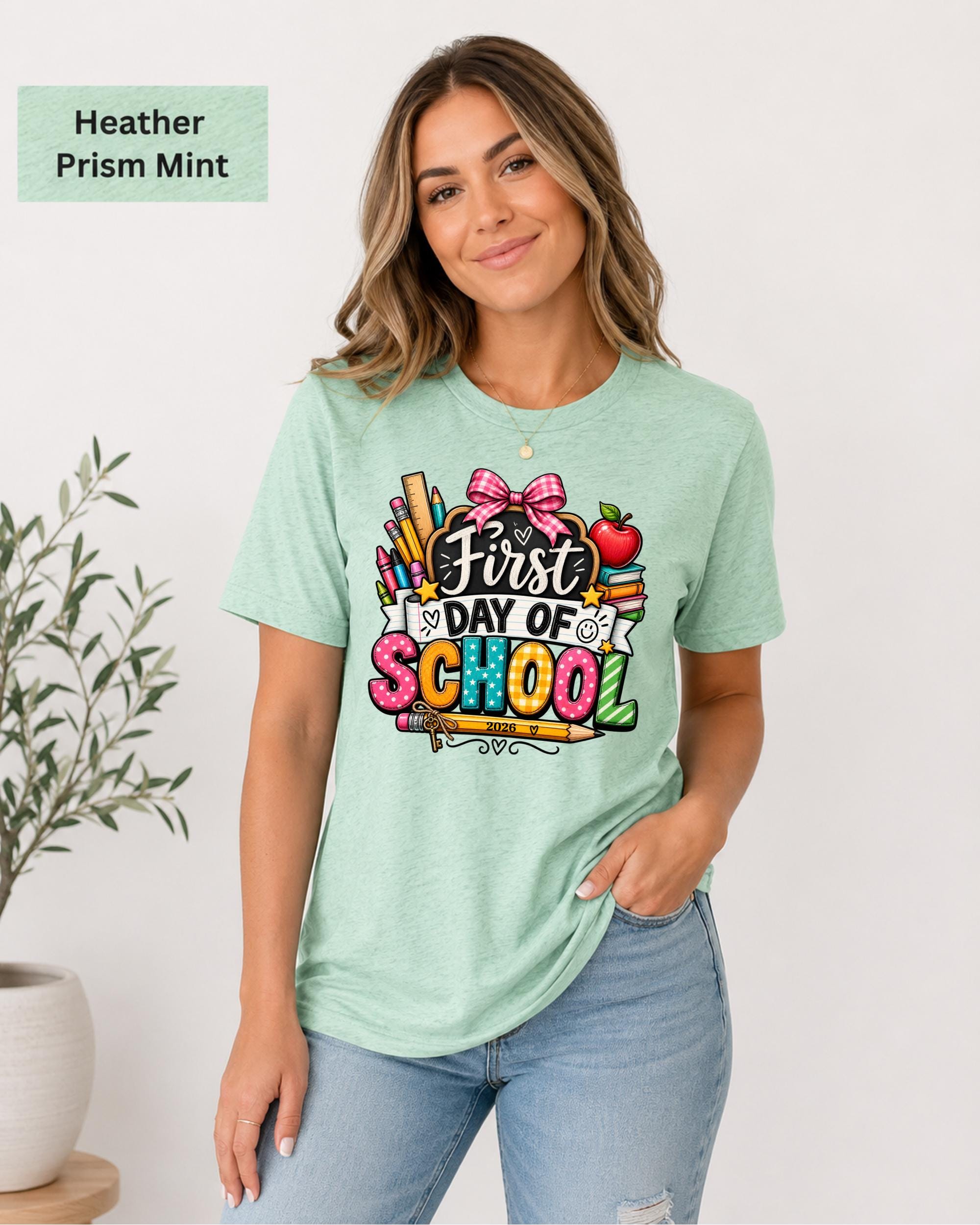 Woman wearing an Heather Prism Bella+Canvas 3001 personalized First Day of School shirt with customizable teacher name and year, colorful pencils, crayons, books, apple, and pink bow design.