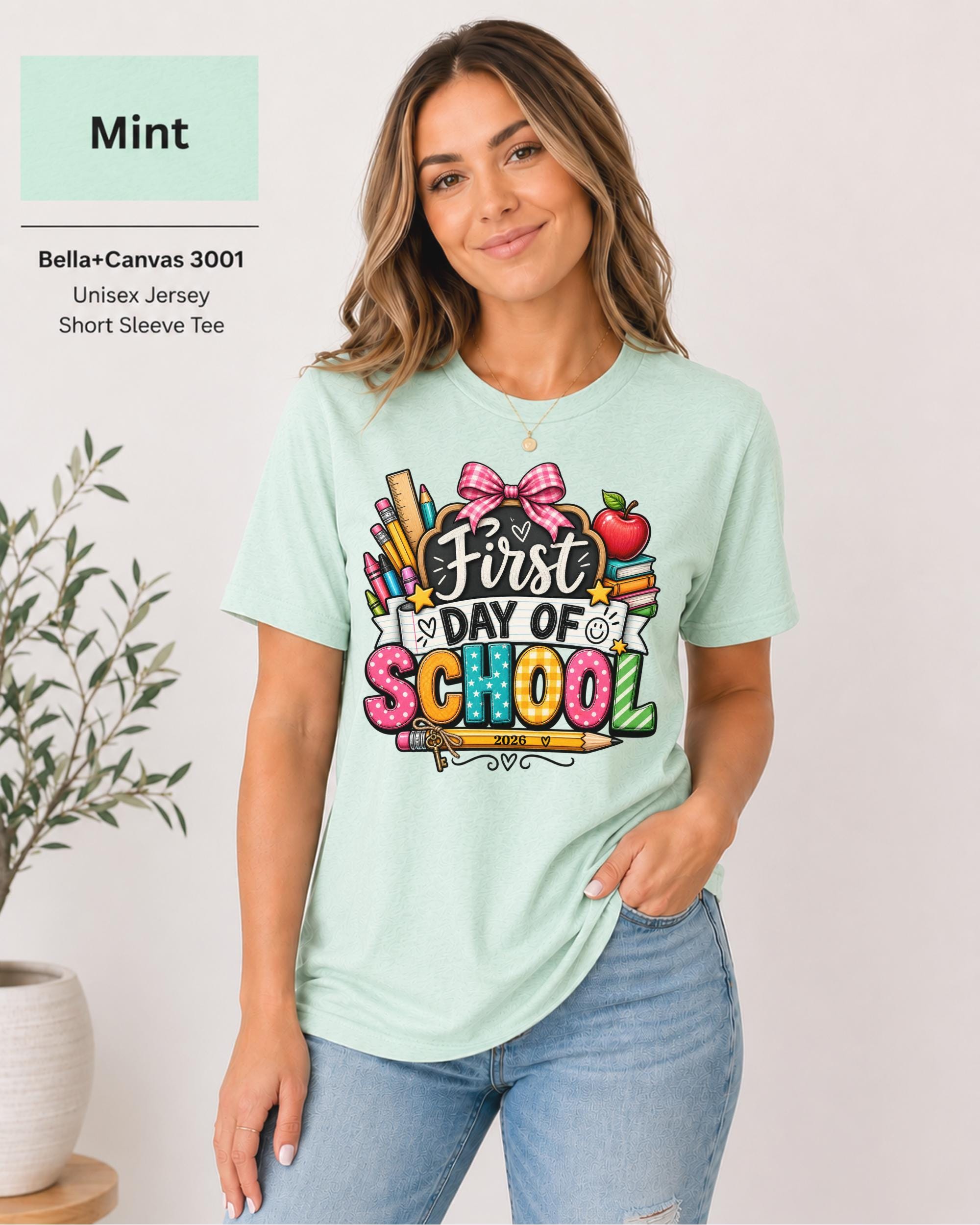 Woman wearing an Mint Bella+Canvas 3001 personalized First Day of School shirt with customizable teacher name and year, colorful pencils, crayons, books, apple, and pink bow design.