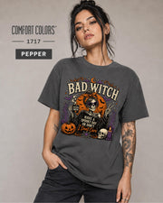 Woman wearing a Pepper Comfort Colors 1717 Bad Witch Halloween shirt with skeleton artwork.