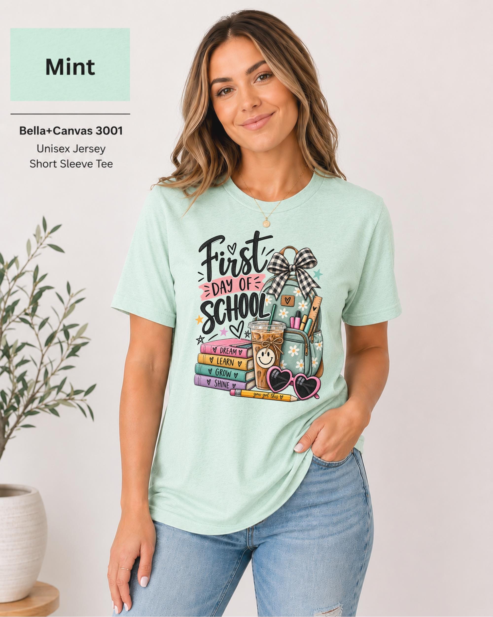 Woman wearing a Mint Bella+Canvas 3001 First Day of School teacher shirt with colorful classroom artwork.