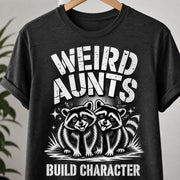 Dark charcoal T-shirt on a hanger featuring the Weird Aunts Build Character funny raccoon graphic.