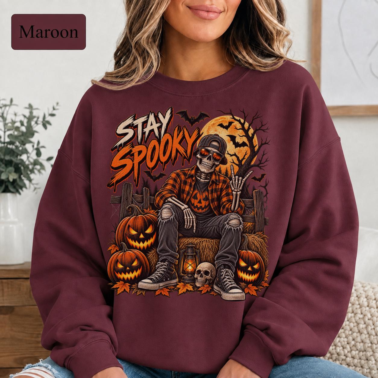 Maroon Halloween sweatshirt featuring a Stay Spooky skeleton graphic with jack-o’-lanterns, full moon, bats, autumn leaves, and orange fall details.