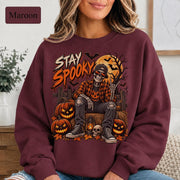 Maroon Halloween sweatshirt featuring a Stay Spooky skeleton graphic with jack-o’-lanterns, full moon, bats, autumn leaves, and orange fall details.