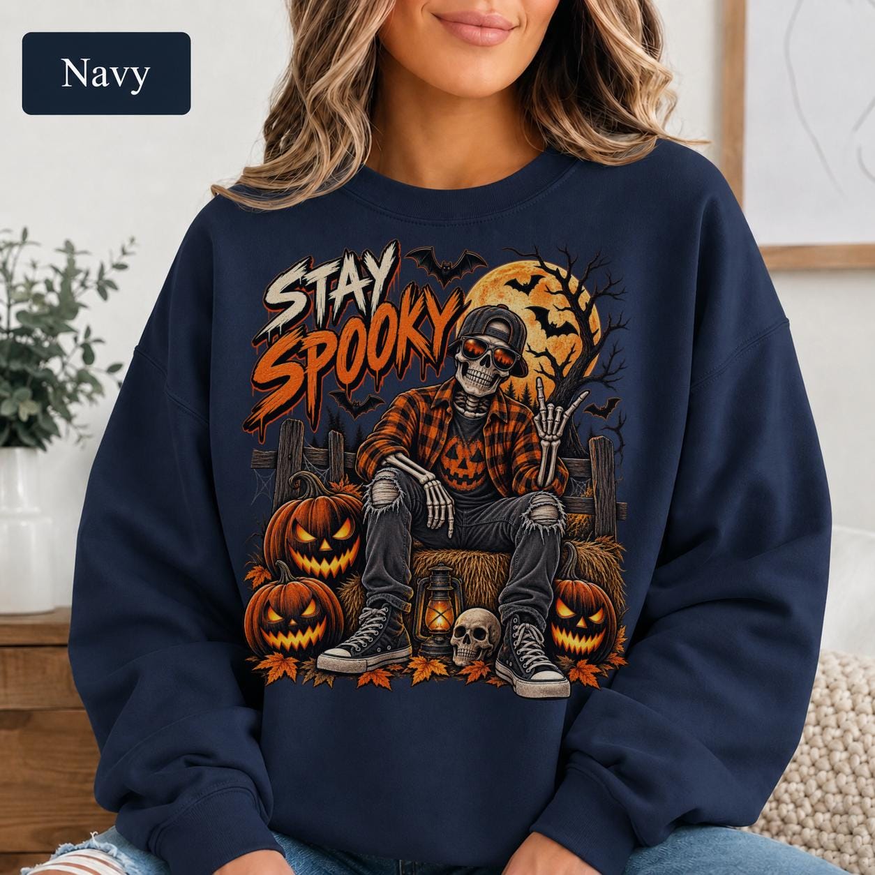 Navy Halloween sweatshirt featuring a Stay Spooky skeleton graphic with jack-o’-lanterns, full moon, bats, autumn leaves, and orange fall details.