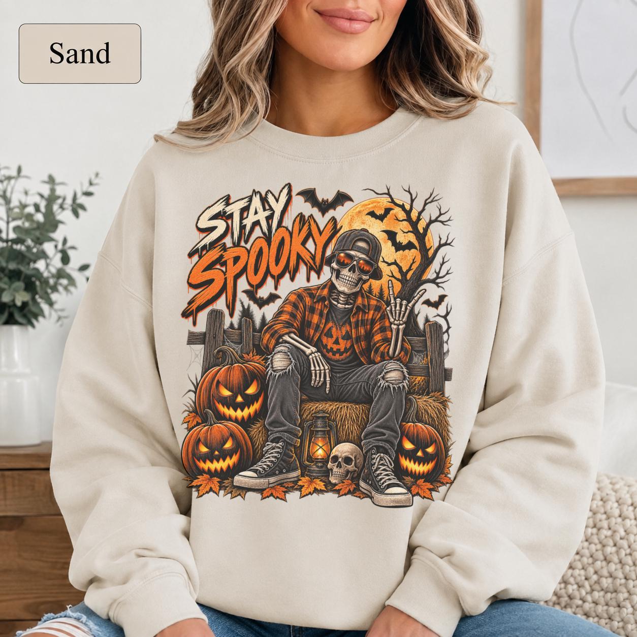 Sand Halloween sweatshirt featuring a Stay Spooky skeleton graphic with jack-o’-lanterns, full moon, bats, autumn leaves, and orange fall details.