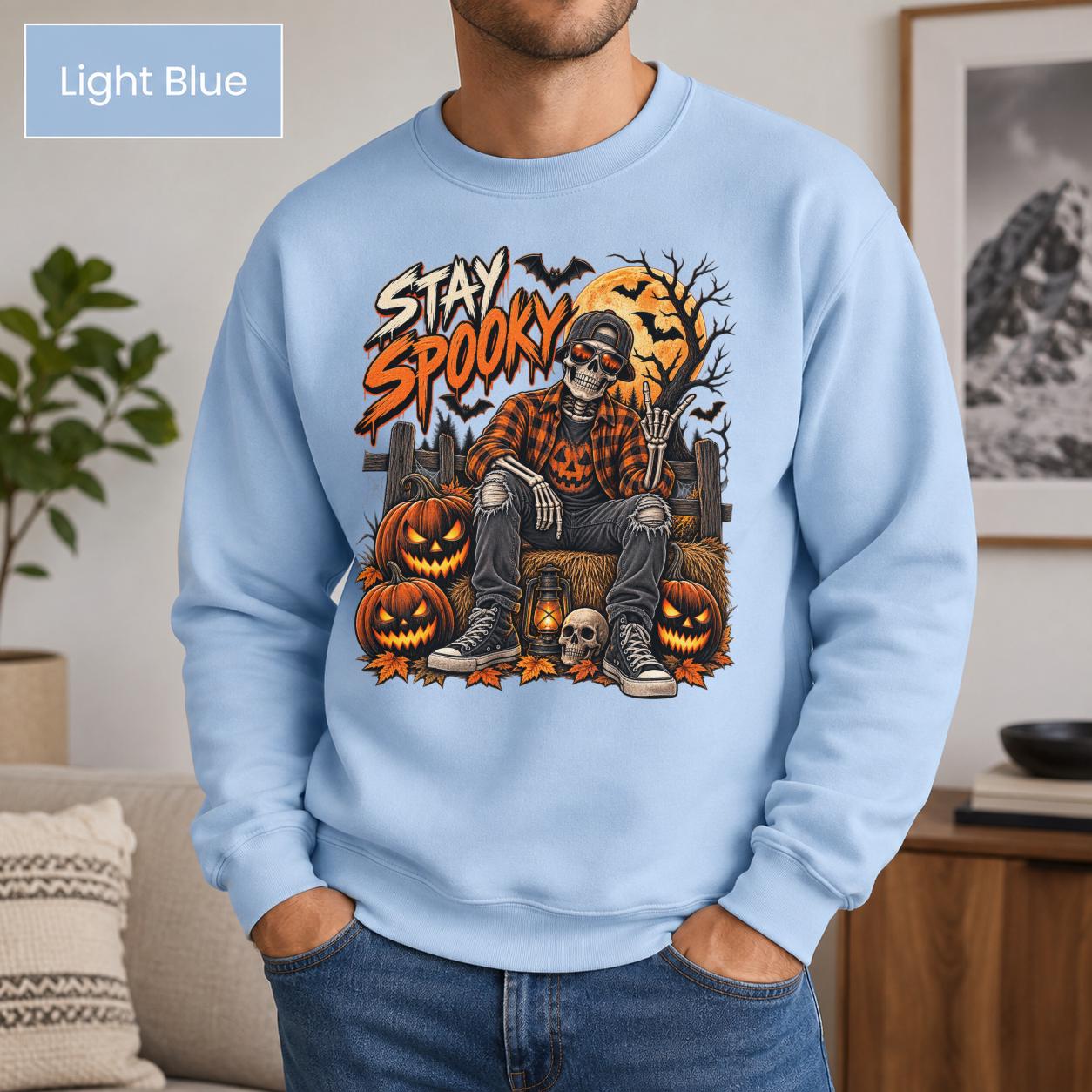 Light blue Halloween sweatshirt featuring a Stay Spooky skeleton graphic with jack-o’-lanterns, full moon, bats, autumn leaves, and orange fall details.