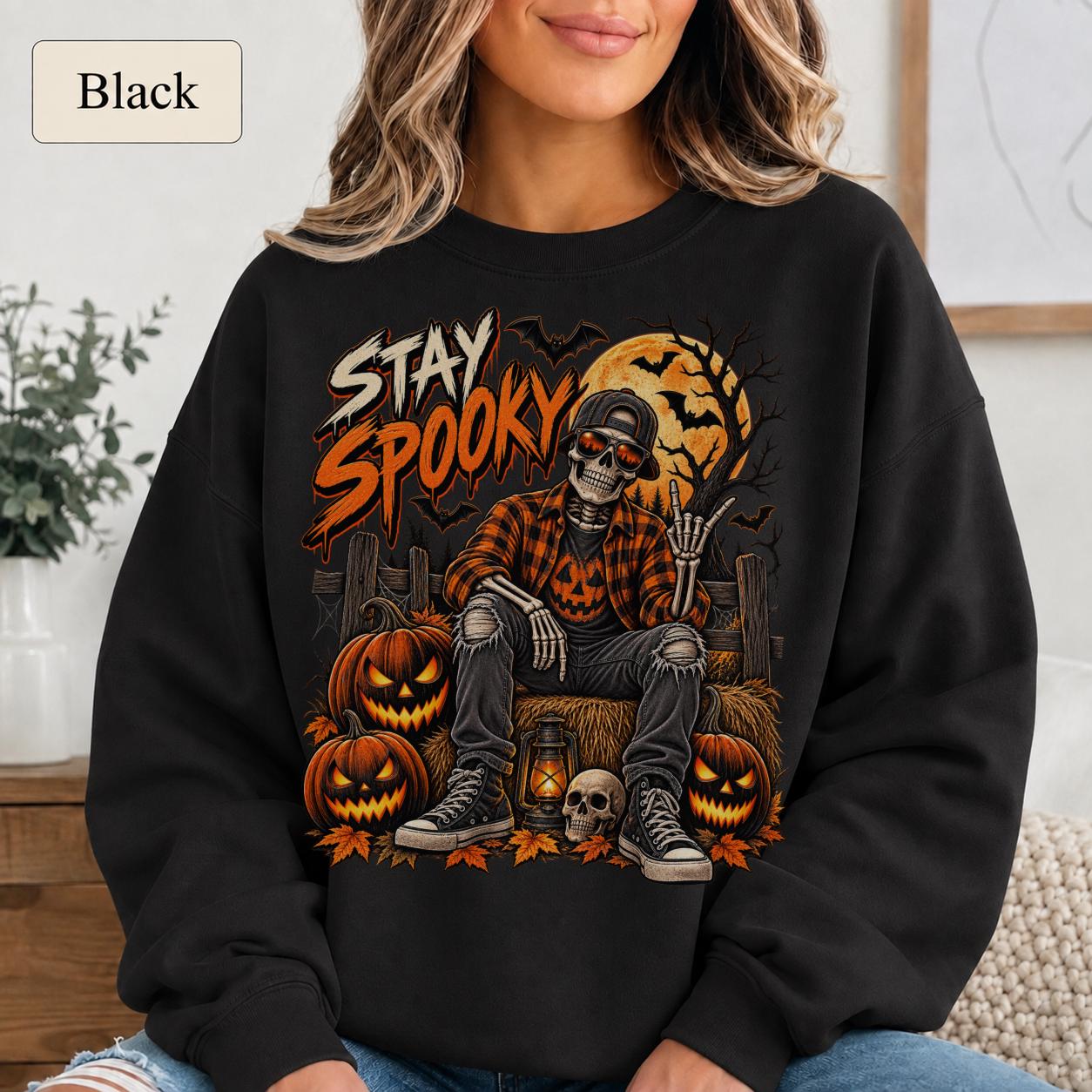Black Halloween sweatshirt featuring a Stay Spooky skeleton graphic with jack-o’-lanterns, full moon, bats, autumn leaves, and orange fall details.