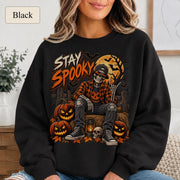 Black Halloween sweatshirt featuring a Stay Spooky skeleton graphic with jack-o’-lanterns, full moon, bats, autumn leaves, and orange fall details.