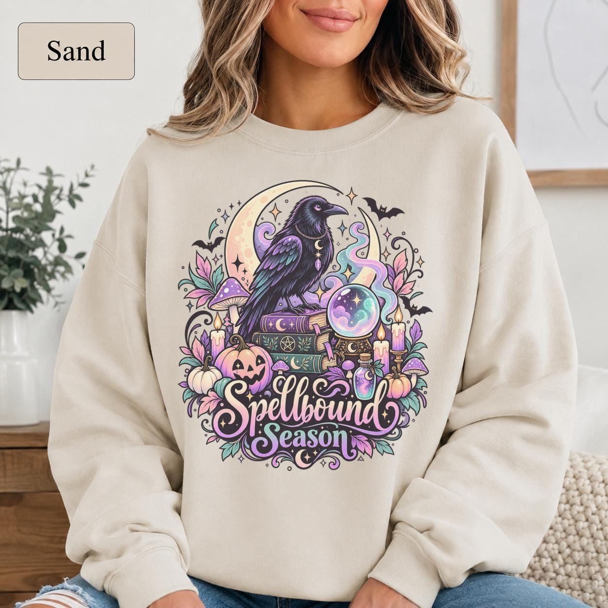 Pastel Halloween sweatshirt featuring raven, crescent moon, spell books, candles, and crystal ball artwork.
