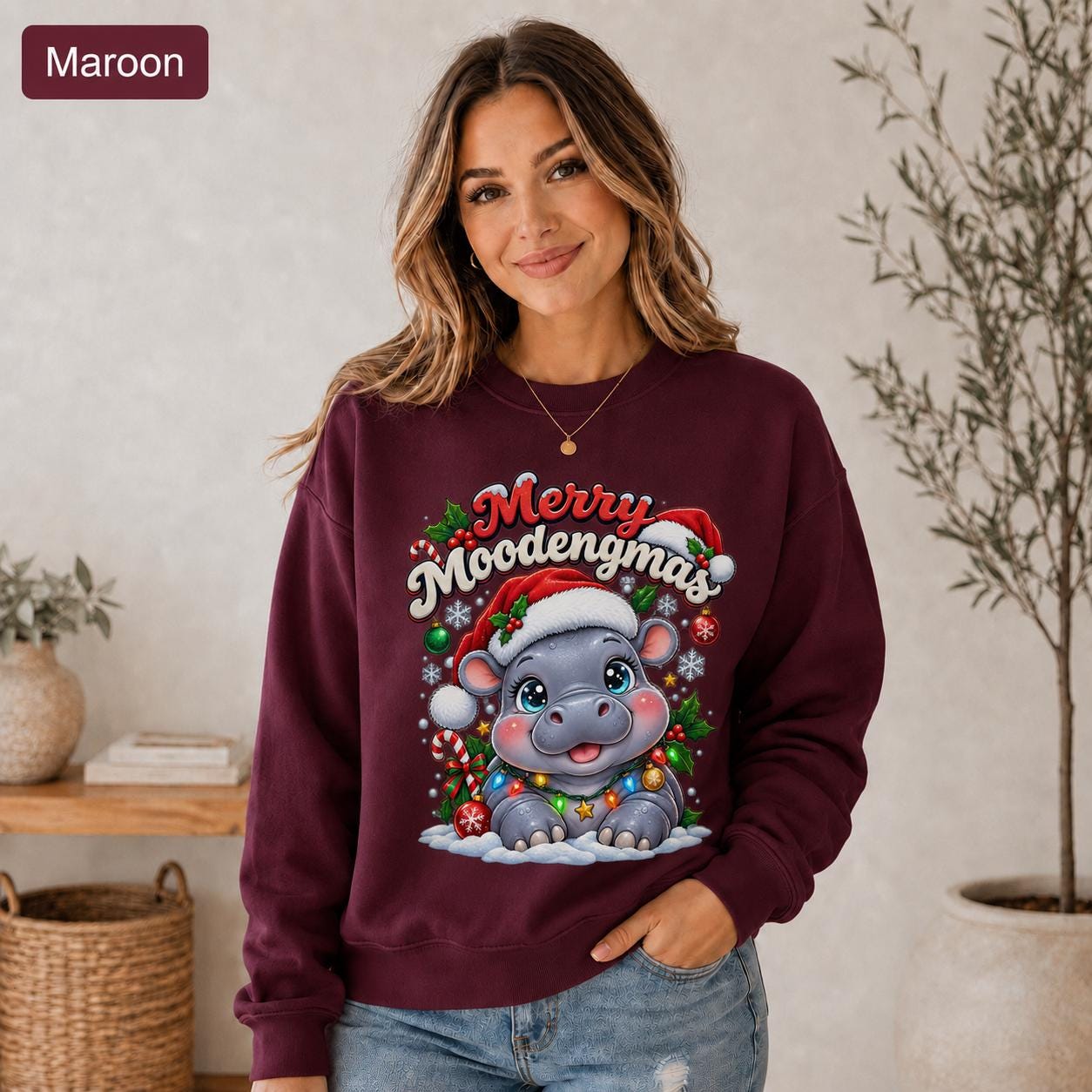 Maroon Christmas sweatshirt featuring a cute hippo in a Santa hat with Merry Moodengmas text, candy canes, ornaments, holly, and snowflakes.
