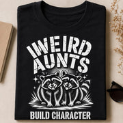 Black T-shirt flat lay featuring the Weird Aunts Build Character raccoon design with bold monochrome artwork.
